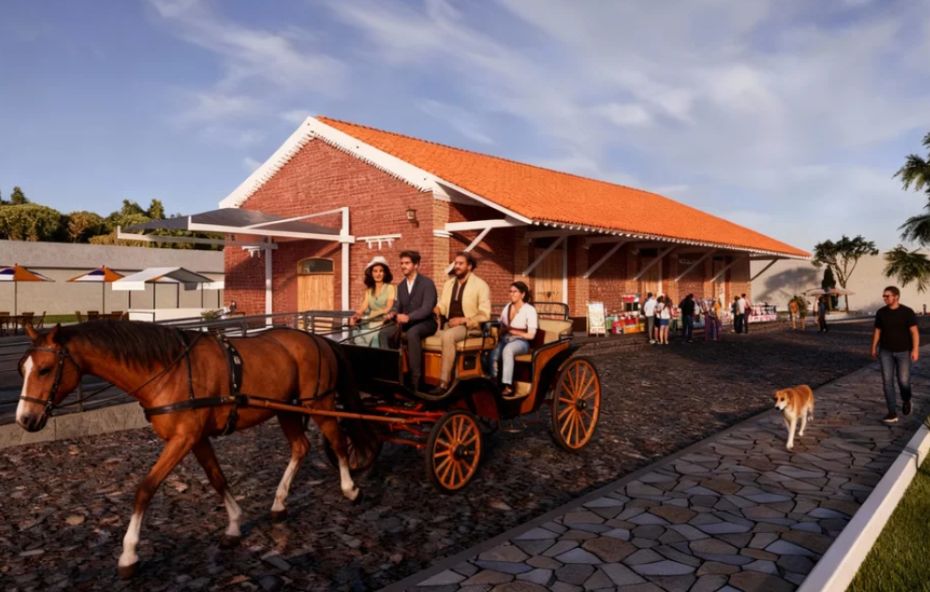 Uma carruagem antiga puxada por um cavalo marrom transporta quatro pessoas sobre uma rua de paralelepípedos em frente à fachada lateral da Estação de Ipiabas restaurada com suas paredes de tijolos vermelhos e telhado de barro sob um céu azul ensolarado.