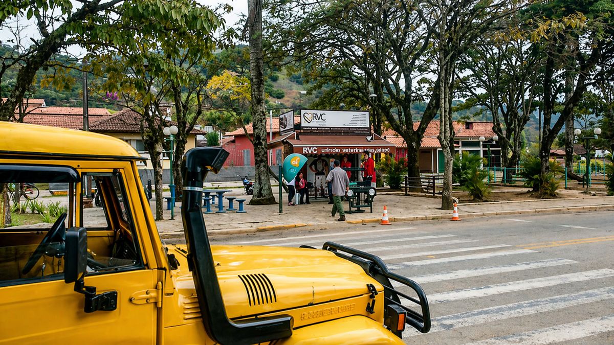 Rua arborizada de Ipiabas com veículo amarelo em primeiro plano, pedestres na calçada e comércio local ao fundo em um dia claro.