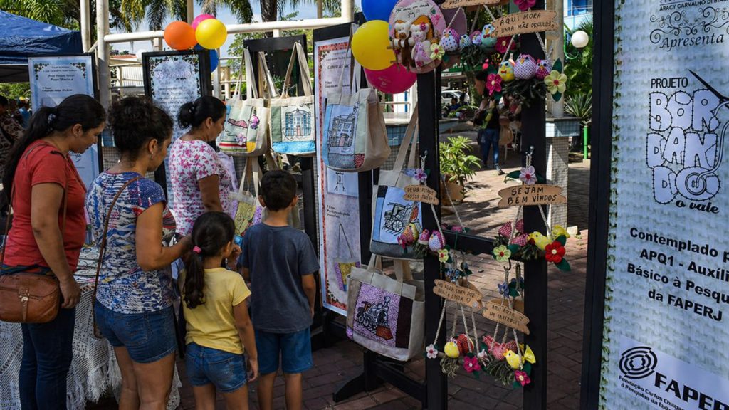 Visitantes observam bolsas artesanais e painéis informativos em uma exposição ao ar livre no pátio do Centro Cultural Aracy Carvalho Di Biase.