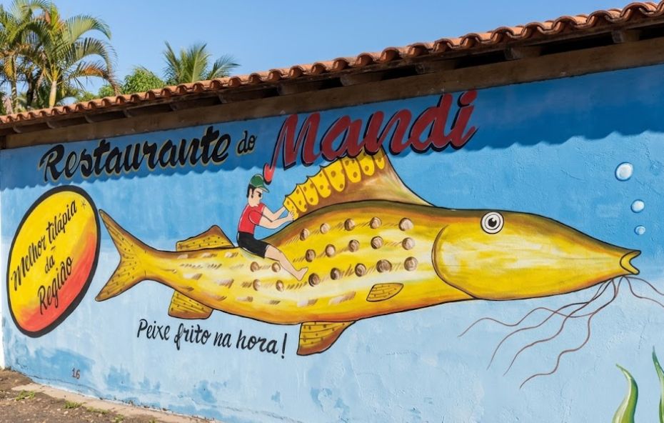 Fotografia de um muro azul com pintura artística de um peixe amarelo gigante e a inscrição Restaurante do Mandi.