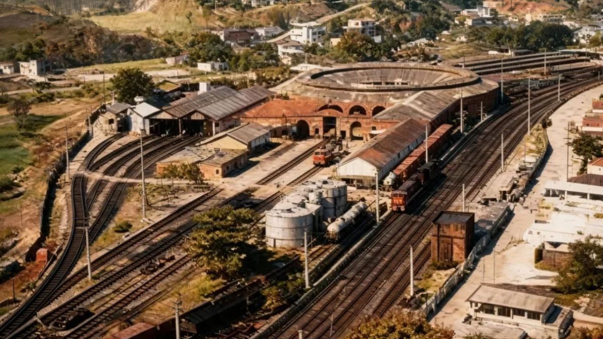 Fotografia aérea colorida mostrando um grande pátio ferroviário com múltiplas linhas de trem e uma rotunda circular em Barra do Piraí.