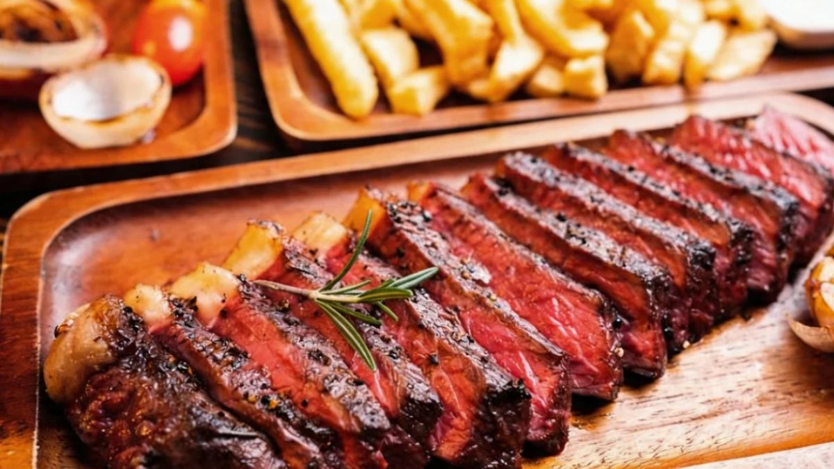 Picanha fatiada em tiras grossas sobre uma tábua de madeira rústica com batatas fritas douradas e vegetais grelhados ao fundo.