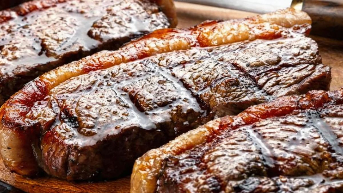 Três bifes de picanha suculentos com capa de gordura dourada e marcas de grelha brilhantes dispostos sobre uma tábua de madeira.