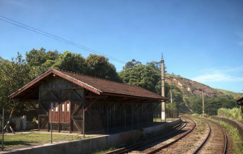 Pequena estação de trem construída em madeira escura com telhado colonial ao lado de trilhos que fazem uma curva suave entre morros e vegetação em Mendes.