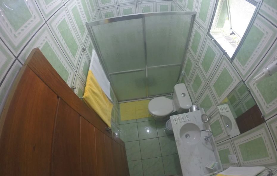 Banheiro privativo com box de vidro, pia em granito, vaso sanitário, toalhas limpas e janela com iluminação natural.