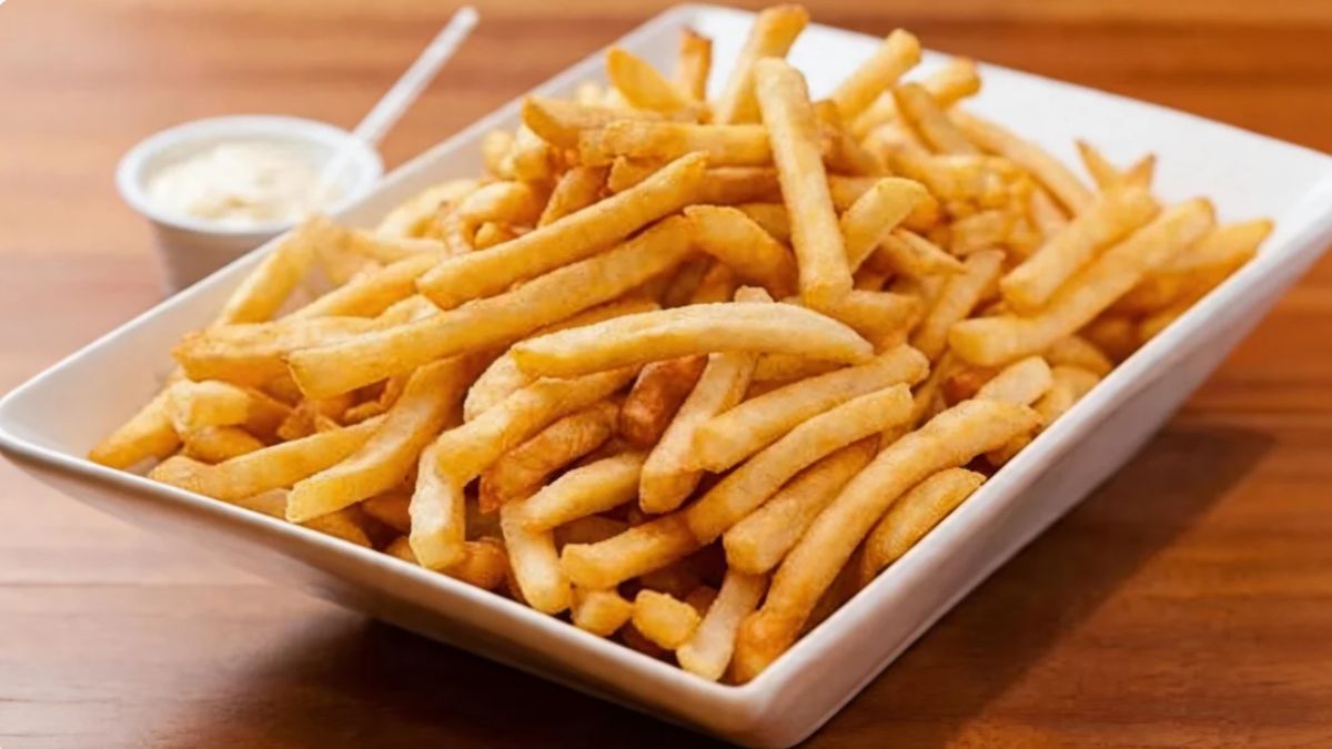 Uma travessa retangular branca de cerâmica repleta de batatas fritas douradas e finas posicionada sobre uma mesa de madeira.