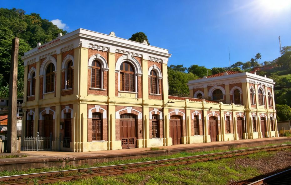 Vista lateral da Estação Ferroviária de Engº Paulo de Frontin com arquitetura de tijolos aparentes e detalhes em branco sob céu azul límpido e luz solar intensa.
