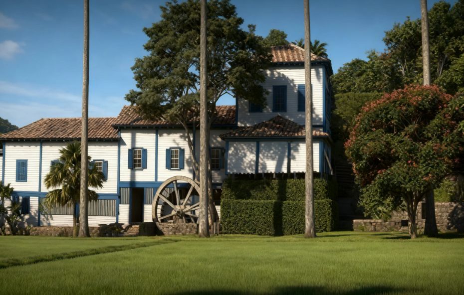 Fotografia de um casarão colonial branco com detalhes em azul apresentando uma grande roda d'água de madeira na lateral e palmeiras imperiais à frente sob um céu limpo.