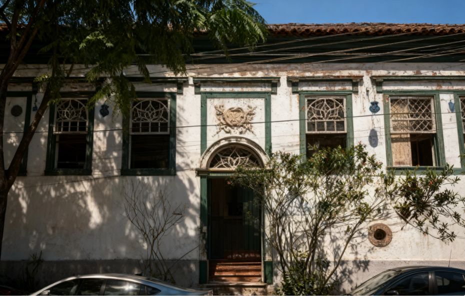 Imagem do interior do Museu da Seresta, com prateleiras e paredes repletas de jornais antigos, fotografias, livros e documentos que contam a história da música. Um cartaz roxo com o título "Conservatória Em Toda Casa Uma Canção" está em destaque.