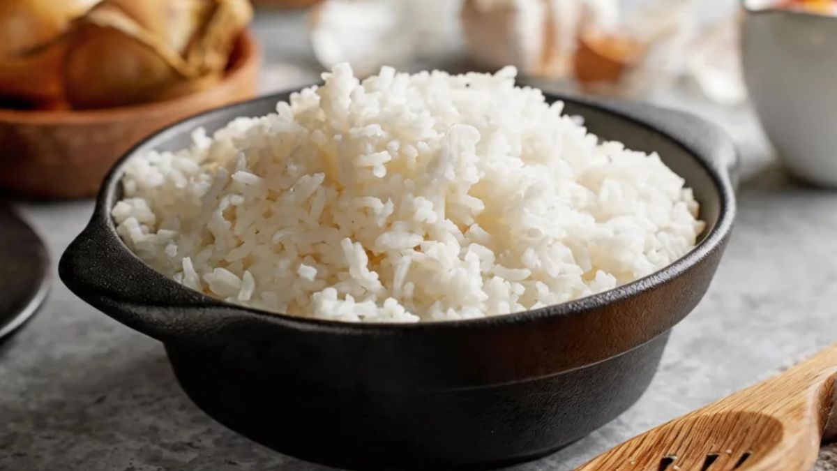 Uma tigela de ferro preta rústica cheia de arroz branco soltinho e fumegante posicionada sobre uma mesa de pedra cinza.