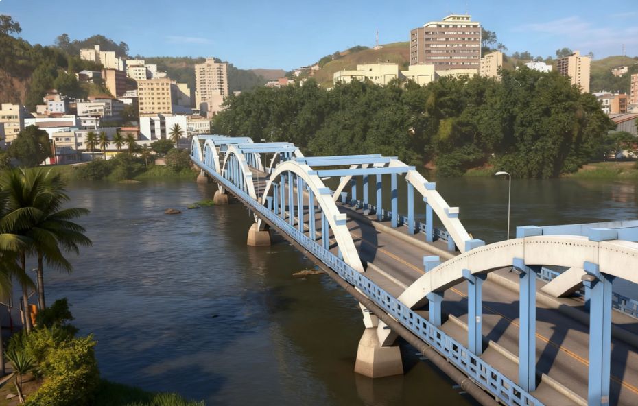 Ponte com estrutura de arcos metálicos nas cores azul e branco atravessando o Rio Paraíba do Sul em Barra Mansa, mostrando edifícios urbanos e morros ao fundo.