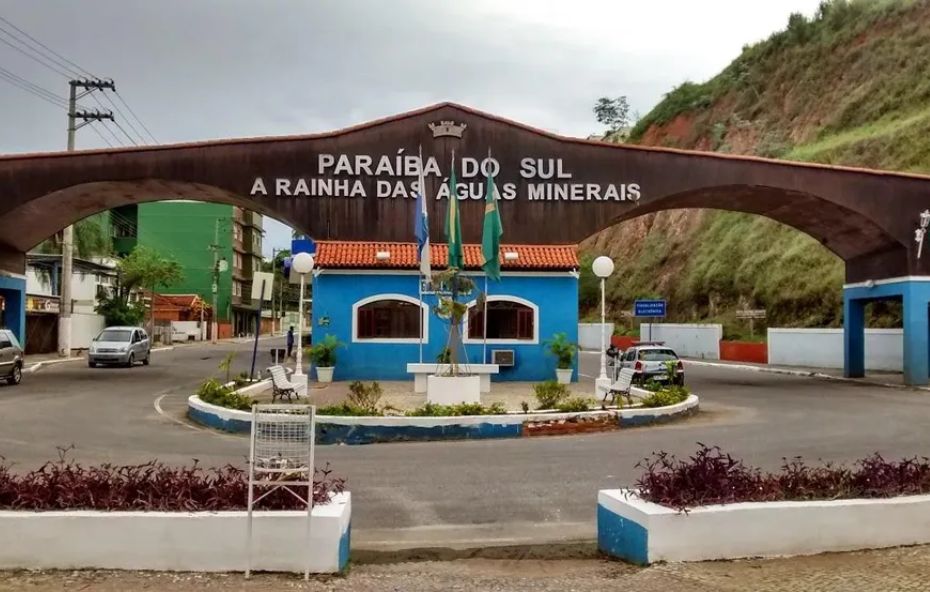 Pórtico de madeira em arco com a inscrição Paraíba do Sul a Rainha das Águas Minerais sobre uma guarita azul e bandeiras hasteadas na entrada da cidade.