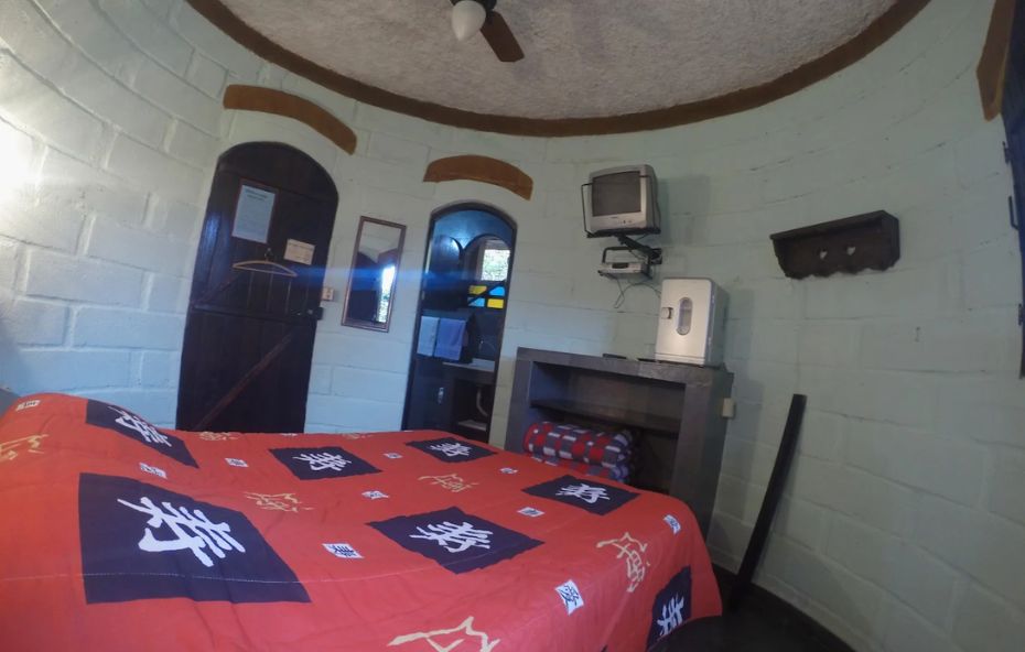 Quarto circular em torre do castelo de Ipiabas com cama de casal, paredes de pedra, teto abobadado e decoração rústica.