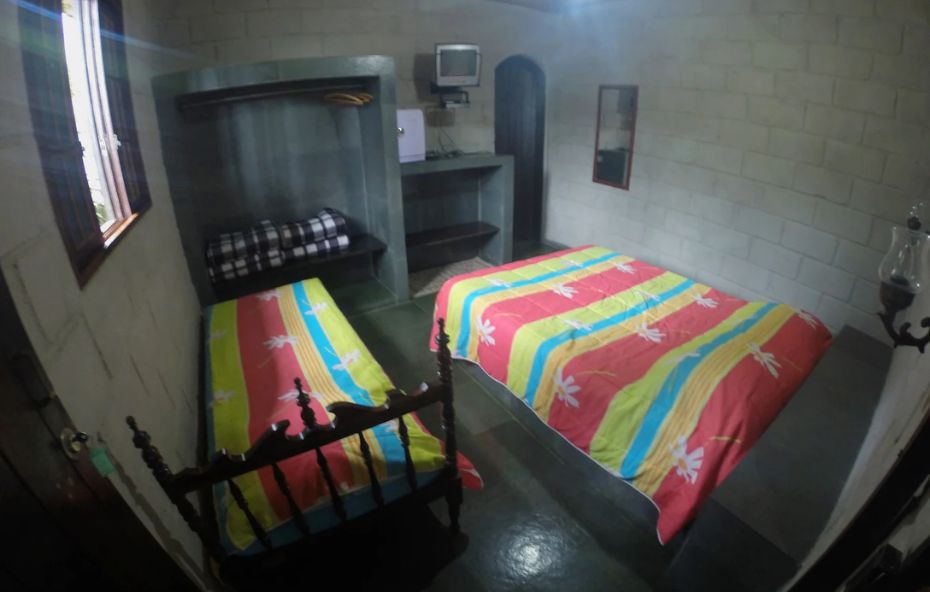 Quarto do castelo de Ipiabas com duas camas, paredes de pedra clara, iluminação natural e decoração simples e confortável.