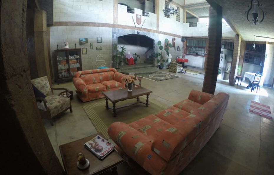 Salão interno do castelo de Ipiabas com pé direito alto, lareira central, brasão na parede, móveis rústicos e iluminação natural.