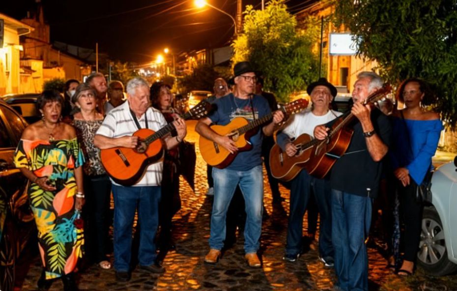 Grupo de músicos homens e mulheres cantando e tocando violões em uma rua de paralelepípedos iluminada à noite em Conservatória.