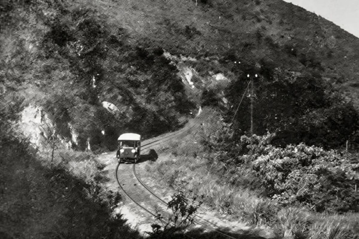 Fotografia histórica em preto e branco de um bonde elétrico percorrendo trilhos de bitola estreita em uma encosta íngreme que liga Ipiabas ao Túnel Velho com vegetação densa e postes de eletrificação.