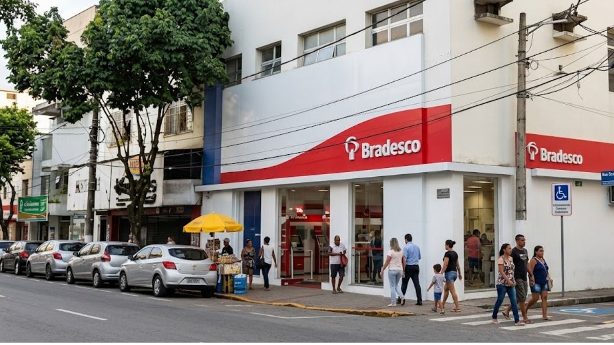 Uma fotografia realista em ângulo médio mostra uma agência bancária Bradesco de esquina branca e vermelha. Há carros estacionados na rua e várias pessoas caminhando na calçada na frente e ao lado da entrada. Um carrinho de comida com um guarda-chuva amarelo está estacionado à esquerda.