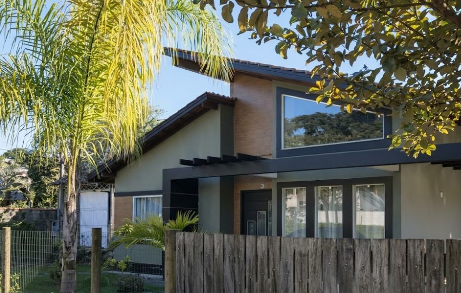 Fachada de casa moderna com linhas retas em tons de cinza e madeira integrada a um jardim com palmeira.