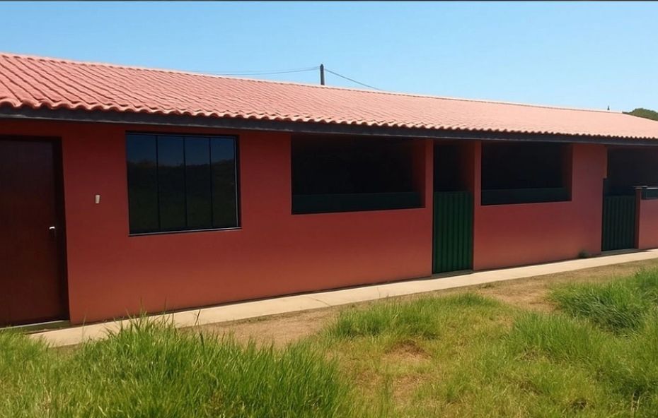 Fachada de uma casa térrea alongada com paredes em tom terracota e telhado cerâmico cercada por gramado verde sob céu azul.