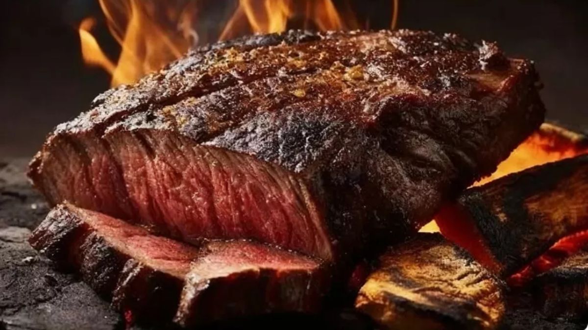 Fotografia em close de uma picanha suculenta sendo grelhada na brasa com chamas ao fundo evidenciando a crosta dourada externa.