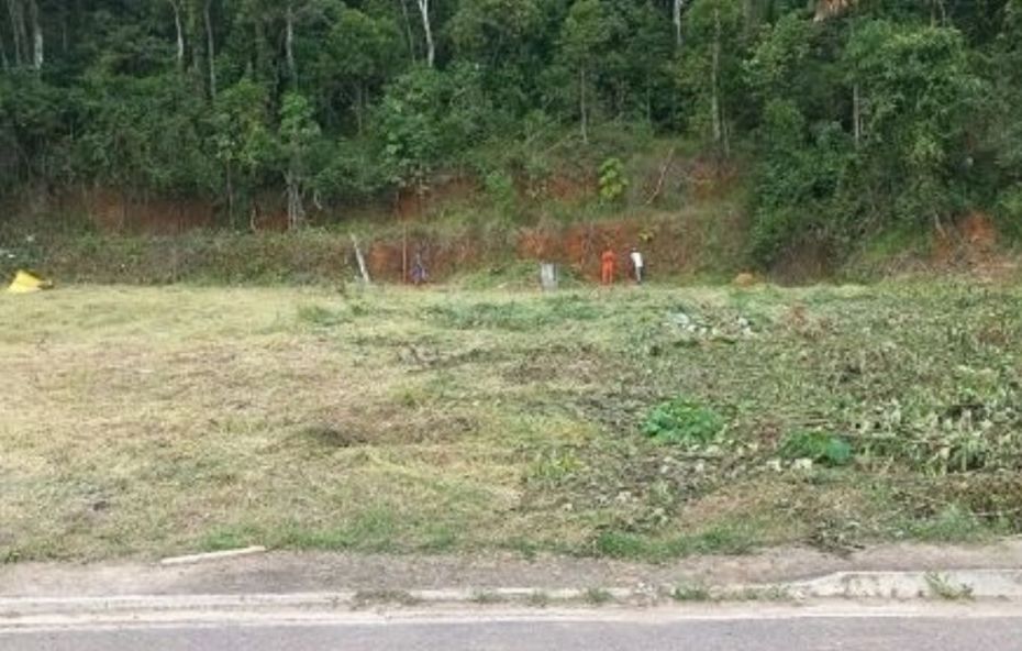 Vista frontal de um amplo terreno gramado com área plana em primeiro plano e um leve aclive ao fundo coberto por vegetação densa.
