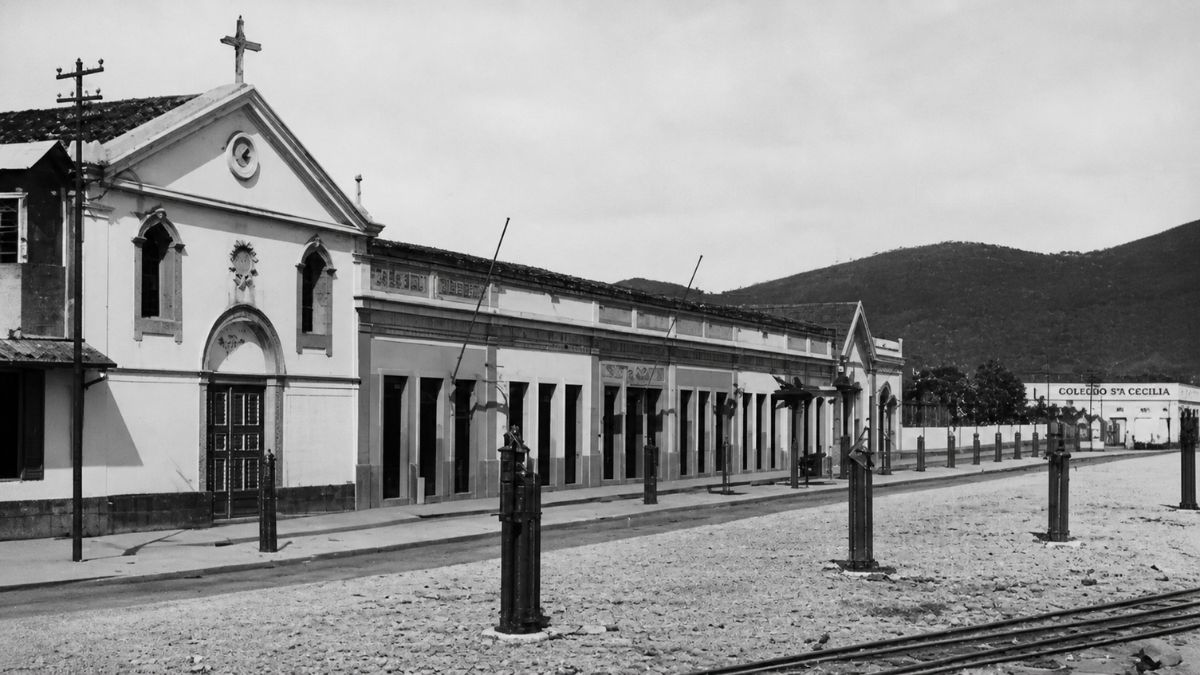 Fotografia em preto e branco de uma capela antiga anexa a um longo prédio.