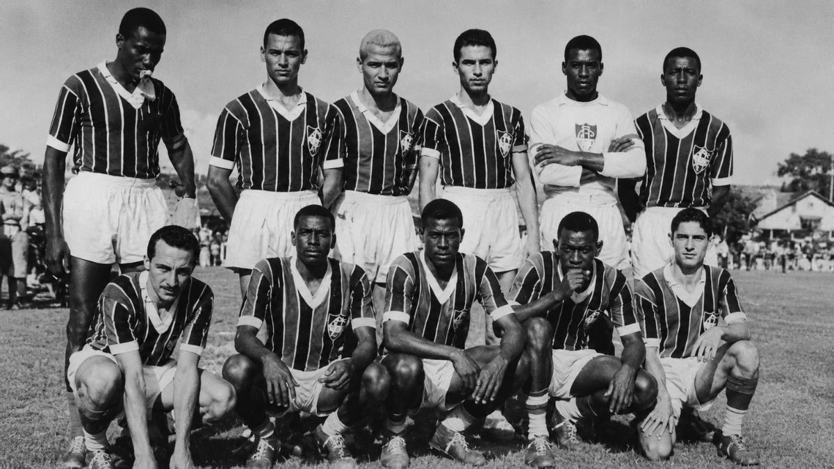 Fotografia em preto e branco de um time de futebol posado uniformizado no campo.