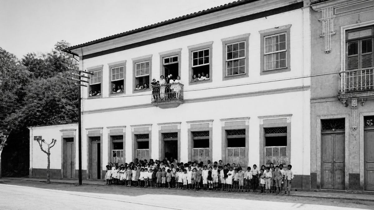 Fotografia em preto e branco de alunos em frente a um casarão de dois andares.
