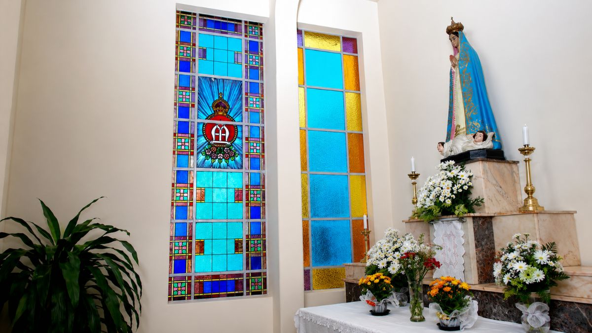 Fotografia de altar com imagem de Nossa Senhora de Fátima ao lado de vitrais coloridos em azul, amarelo e vermelho.
