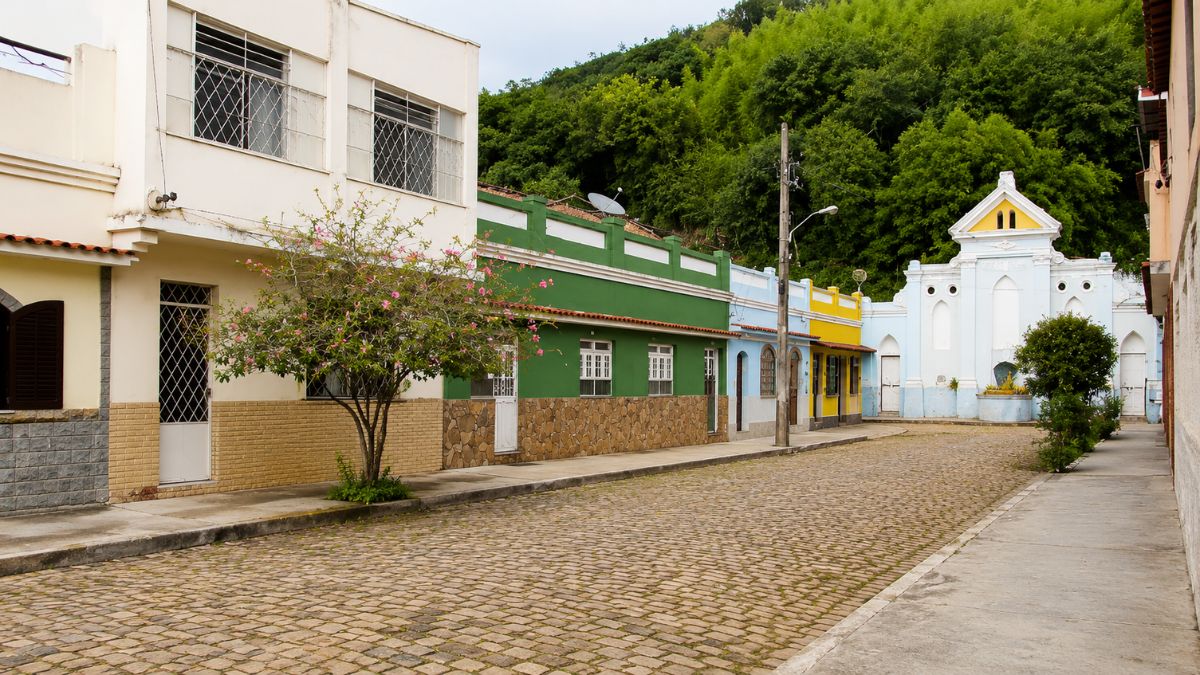 Fotografia de uma rua de paralelepípedos com casas coloridas geminadas que levam ao Chafariz da Carioca ao fundo da via.
