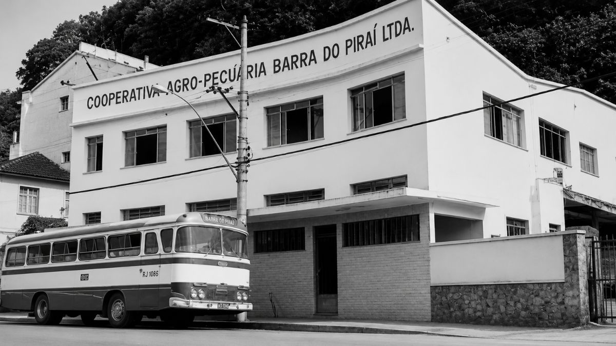 Fotografia em preto e branco de um prédio funcional e um ônibus antigo estacionado.