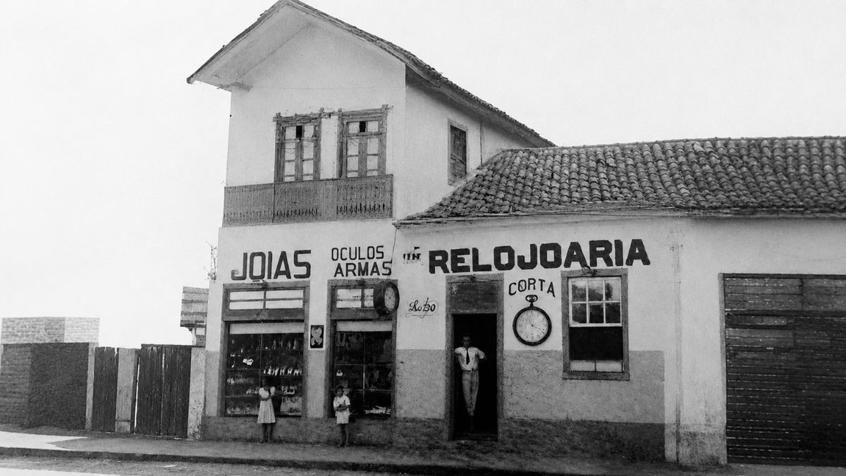 Fotografia em preto e branco de uma relojoaria antiga com letreiros pintados na fachada.