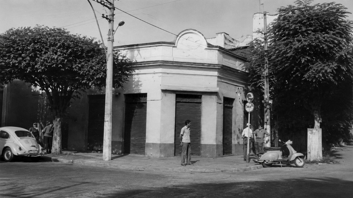 Fotografia em preto e branco de um prédio de esquina com portas de ferro.