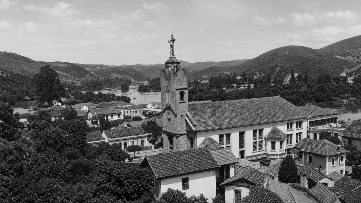 Fotografia em preto e branco de uma igreja com torre sineira e rio ao fundo.