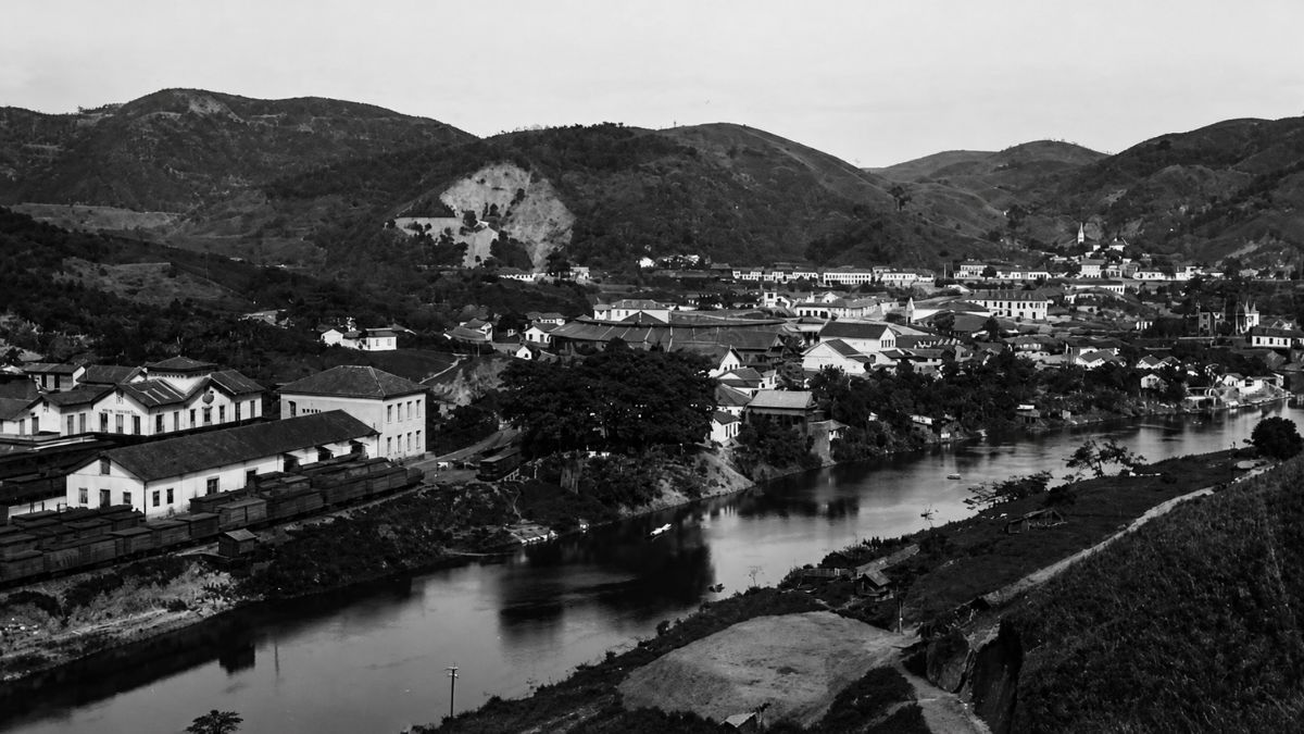 Fotografia aérea em preto e branco de cidade antiga beirando rio entre montanhas.