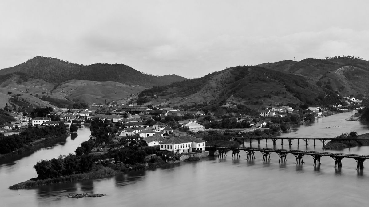 Fotografia aérea em preto e branco de pontes longas sobre o rio e montanhas.