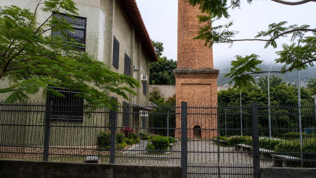 Vista frontal da base quadrada da chaminé de tijolos atrás de um gradil metálico preto ao lado de um prédio.