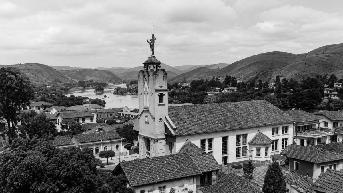 Fotografia em preto e branco de uma igreja com torre alta diante de um rio.