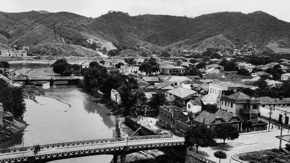 Fotografia em preto e branco de uma ponte urbana cruzando um rio em cidade antiga.