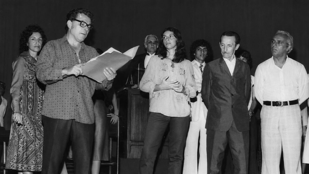 Fotografia em preto e branco de grupo de pessoas reunidas em um palco durante uma apresentação.
