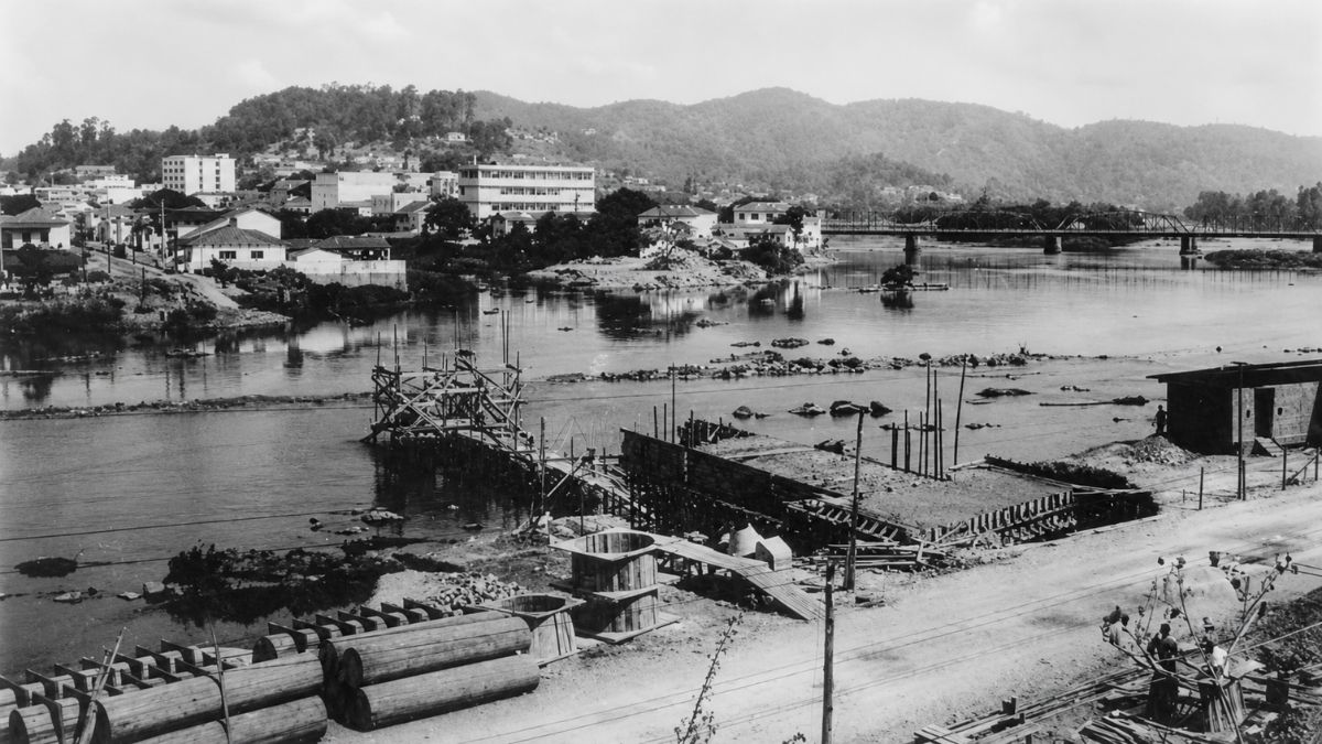 Fotografia em preto e branco mostrando obras de infraestrutura sobre um rio largo.