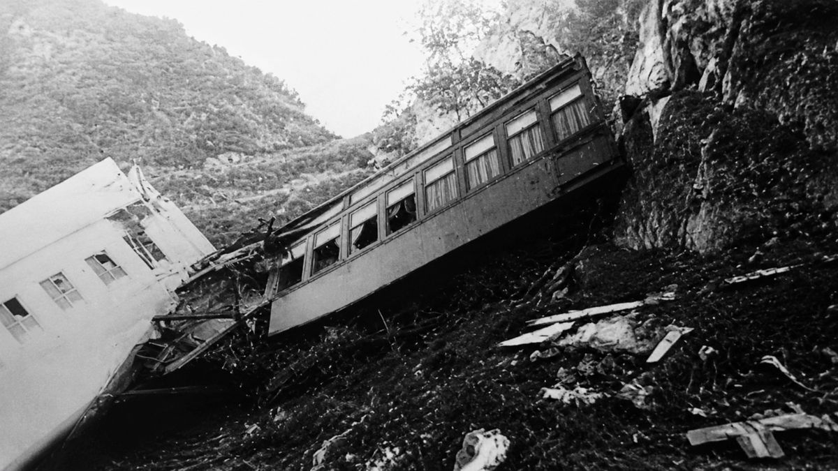 Fotografia em preto e branco mostrando vagões de trem descarrilados em uma encosta íngreme.
