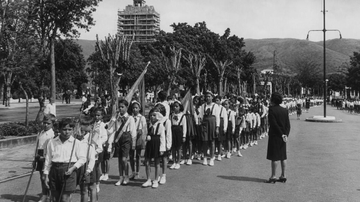 Fotografia em preto e branco de crianças uniformizadas em formação para um desfile escolar.