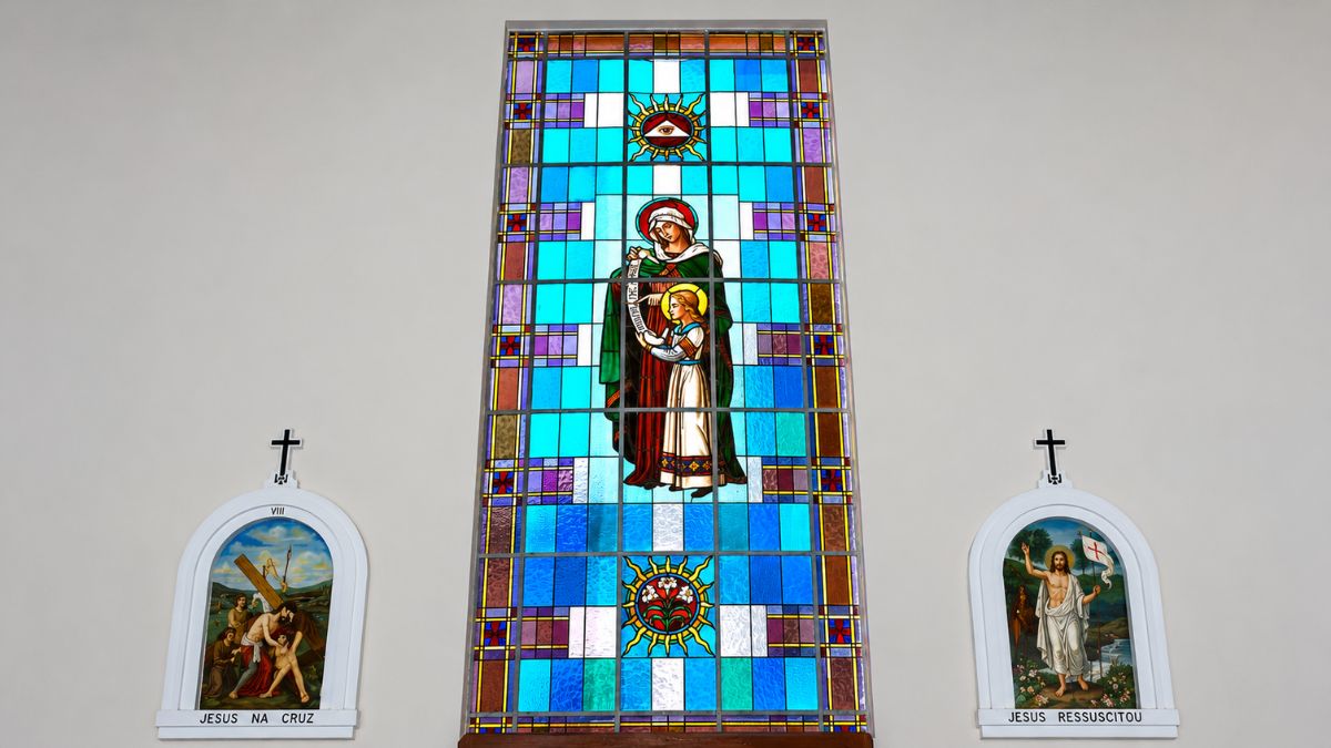 Close de vitral colorido em tons de azul e ciano ladeado por dois quadros em arco da Via Sacra católica.