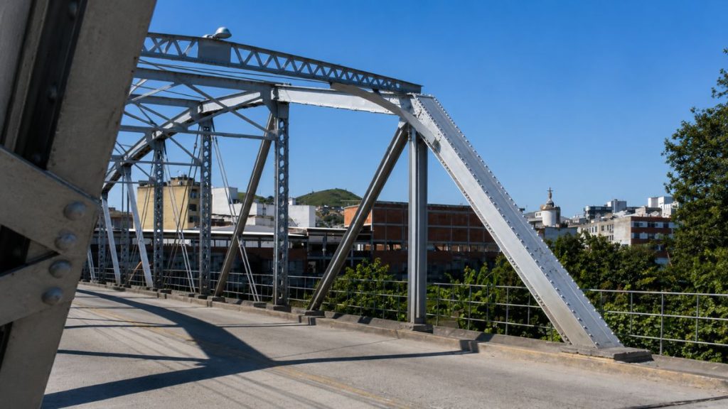 Close lateral da estrutura metálica cinza da Ponte Getúlio Vargas mostrando rebites e vigas com prédios urbanos ao fundo.
