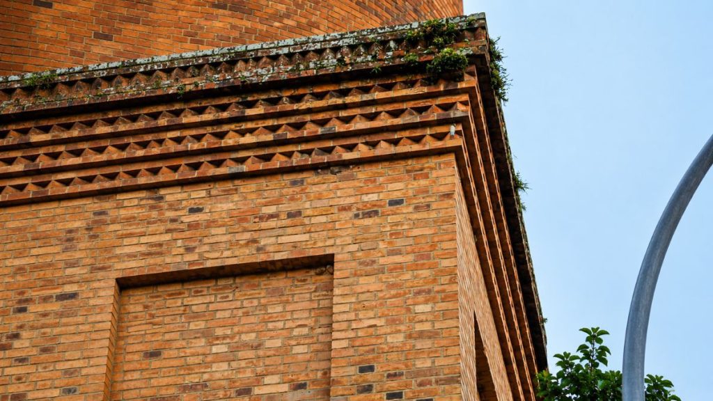 Close nos tijolos avermelhados da base quadrada da chaminé mostrando frisos geométricos em relevo e detalhes decorativos superiores.