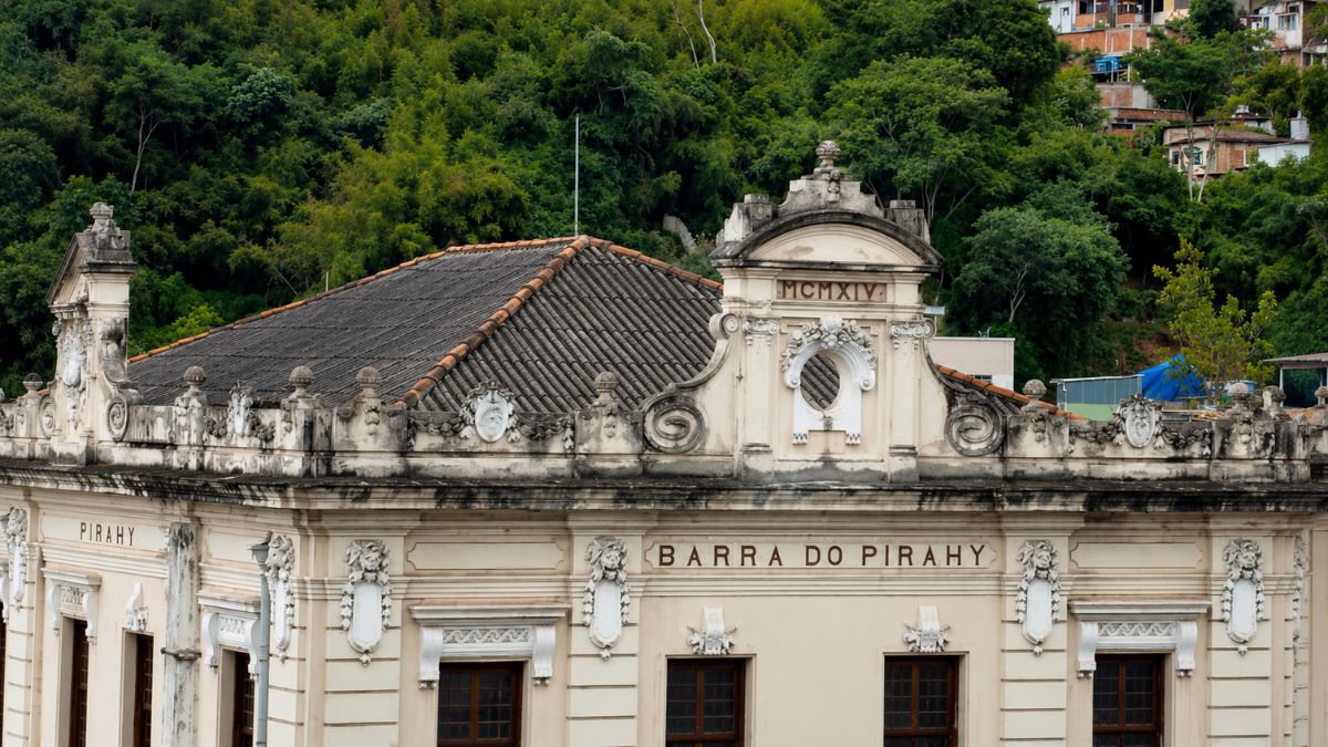 Close do frontão superior de prédio histórico com algarismos romanos e inscrições da cidade sob um telhado de telhas cerâmicas.