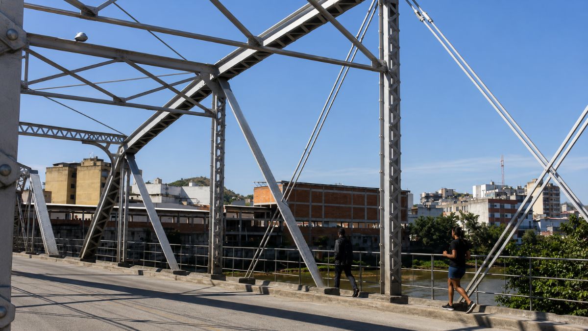 Vista interna da Ponte Getúlio Vargas mostrando treliças metálicas cinzas com pessoas caminhando na lateral sob um céu azul limpo.