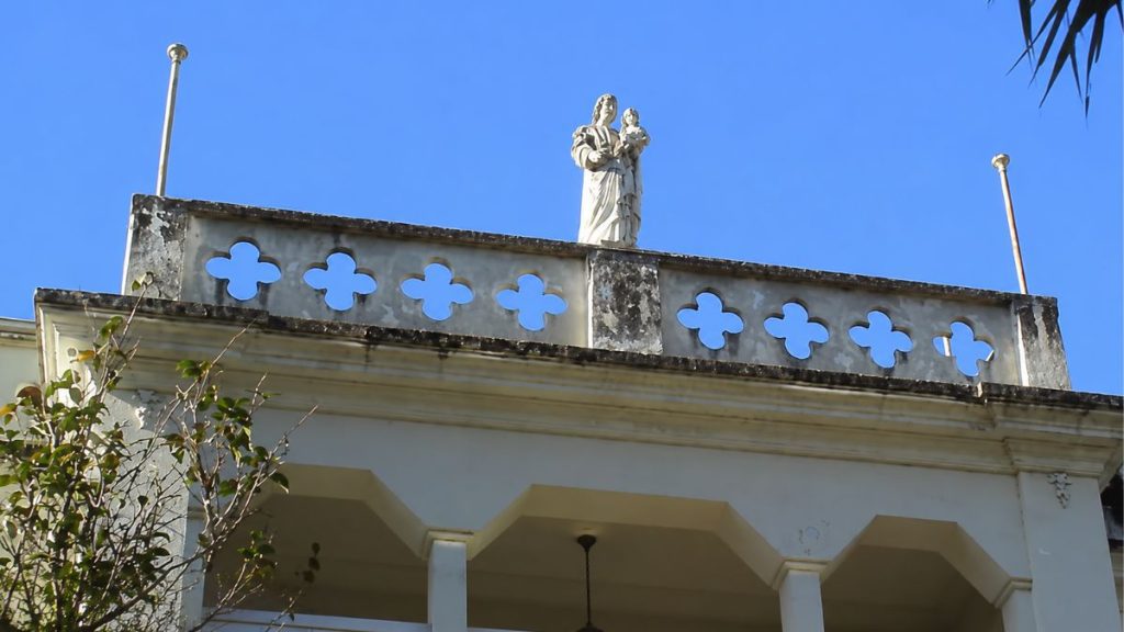 Escultura sacra de São José sobre platibanda com vazados de quadrifólios destacando o coroamento do corpo central sob céu azul.